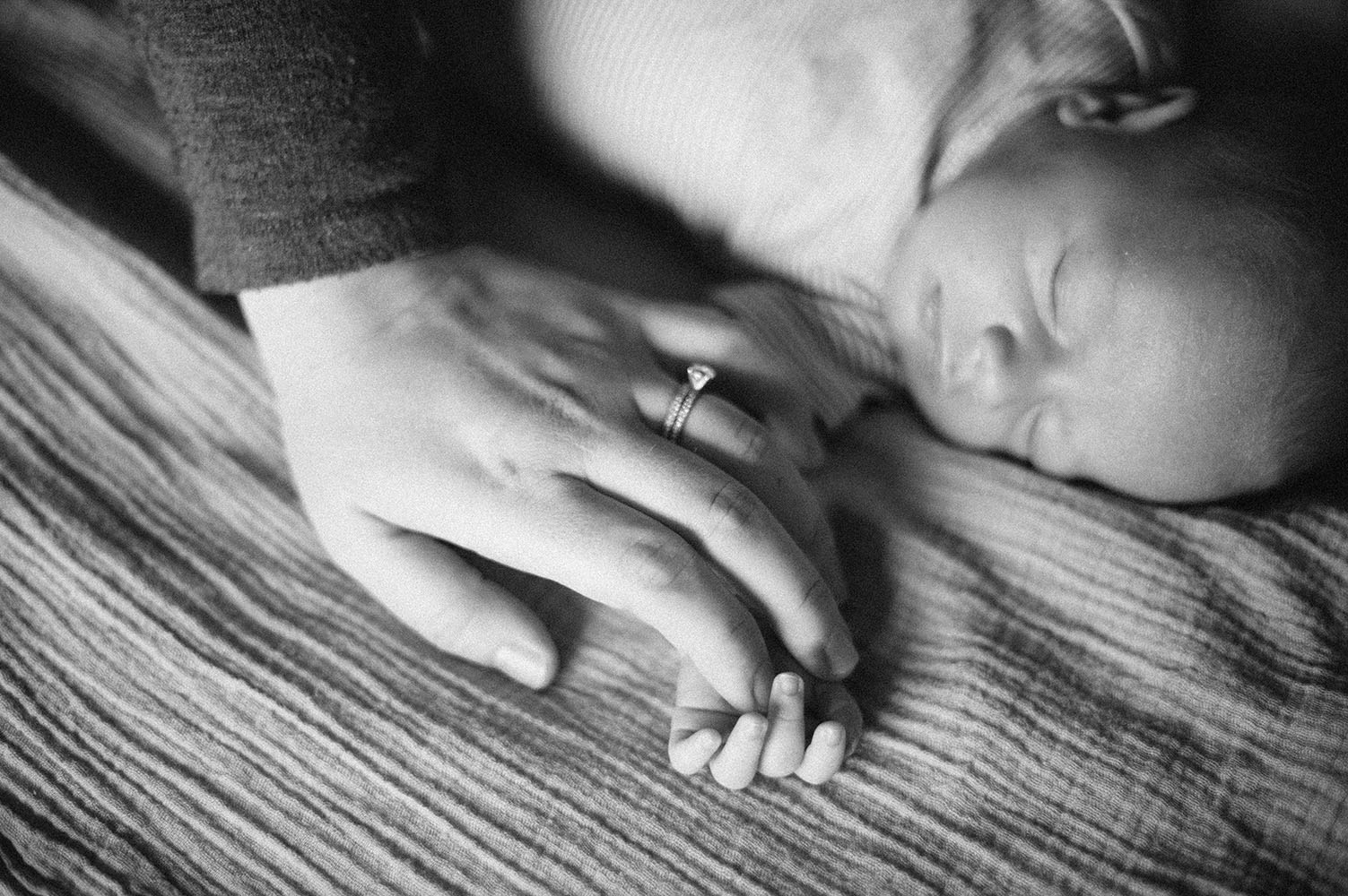 Newborn baby with moms hand wearing wedding ring