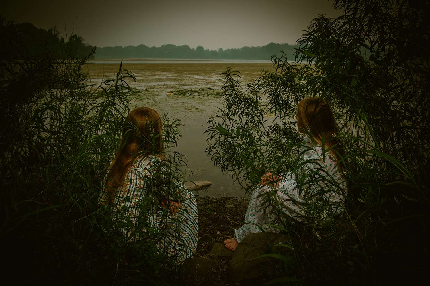 Twin girls sit by a lake in nightgowns with an eerie vibe