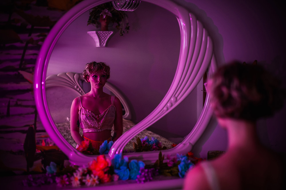 a girl looks at her reflection in a mirror in pink light