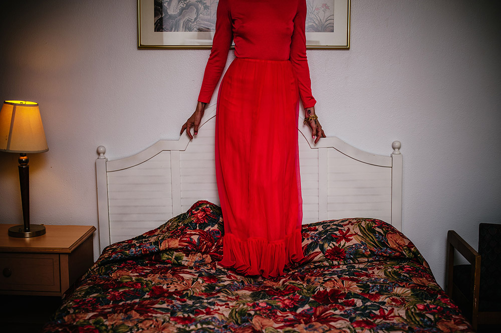a woman stands on an old motel bed in a pink vintage dress but you can't see her head