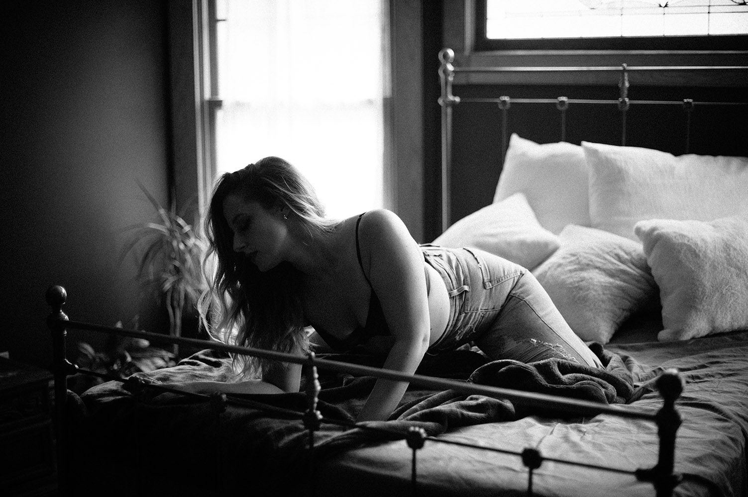 black and white boudoir woman in jeans on bed