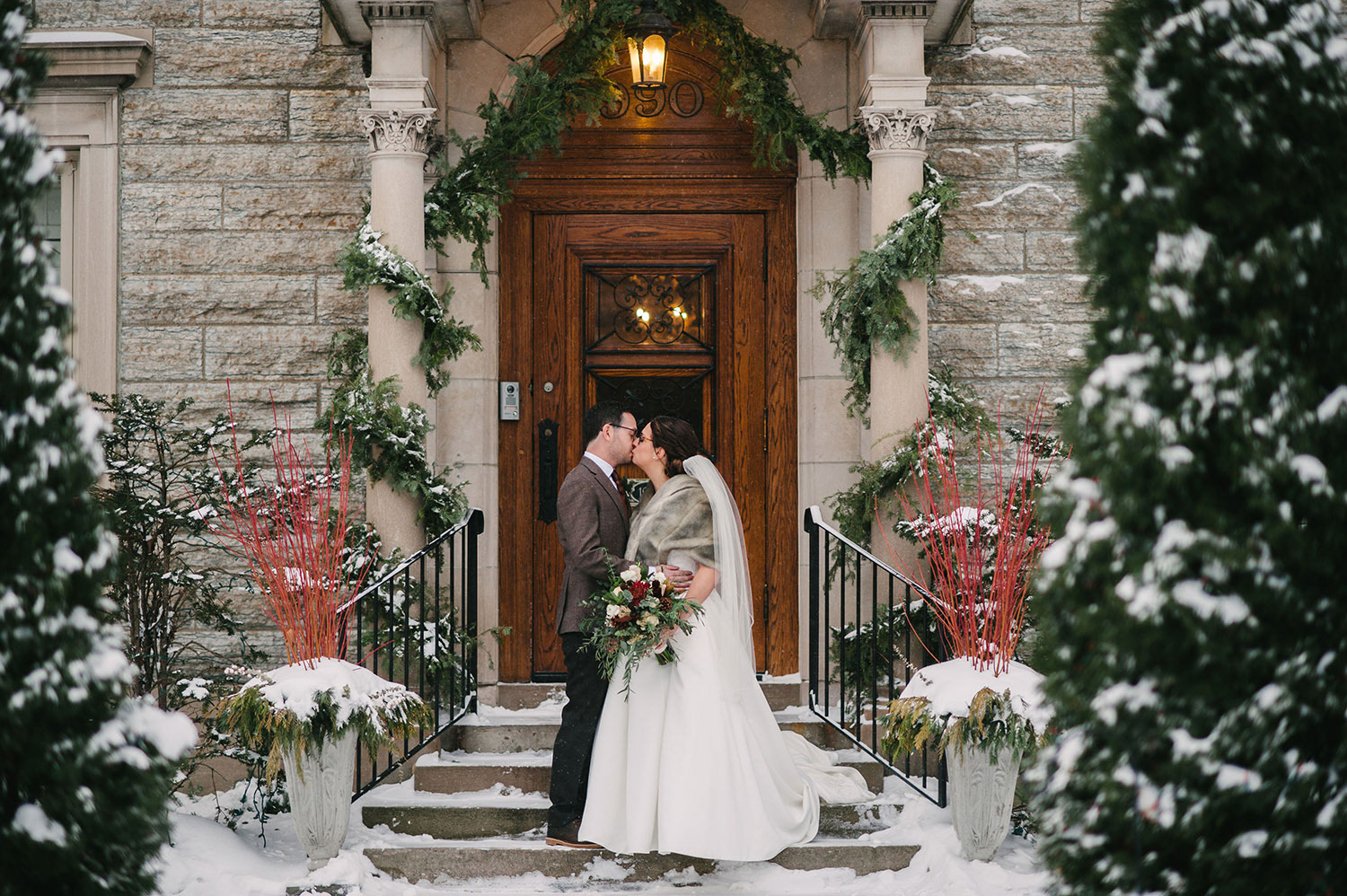 a white couple just married in the snow in front of the Saint Paul College Club kissing