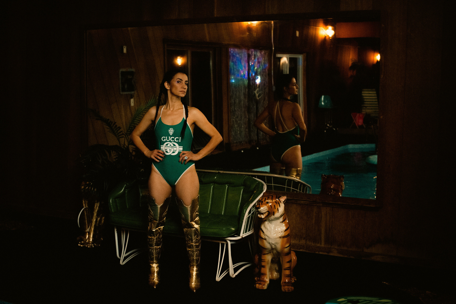 a Hispanic woman in a green Gucci swimsuit by a ceramic tiger at Grandpas Pool House