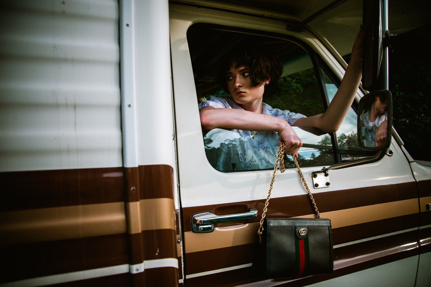 a white woman looking outside an RV window with a purse