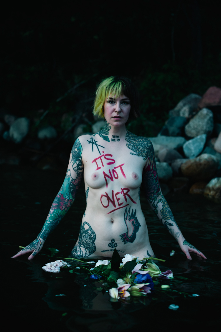 a naked white woman standing in a lake with the words it's not over written on her body at the Zebra house