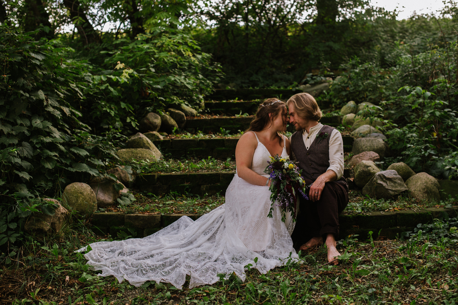 a married couple sitting next to each other on steps in a forest