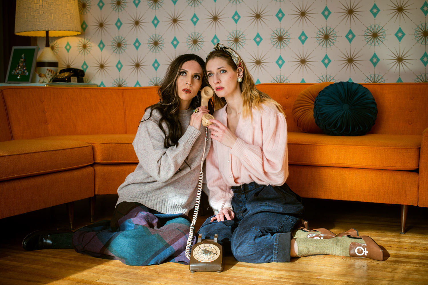 two girls sitting in front of orange couch holding a phone