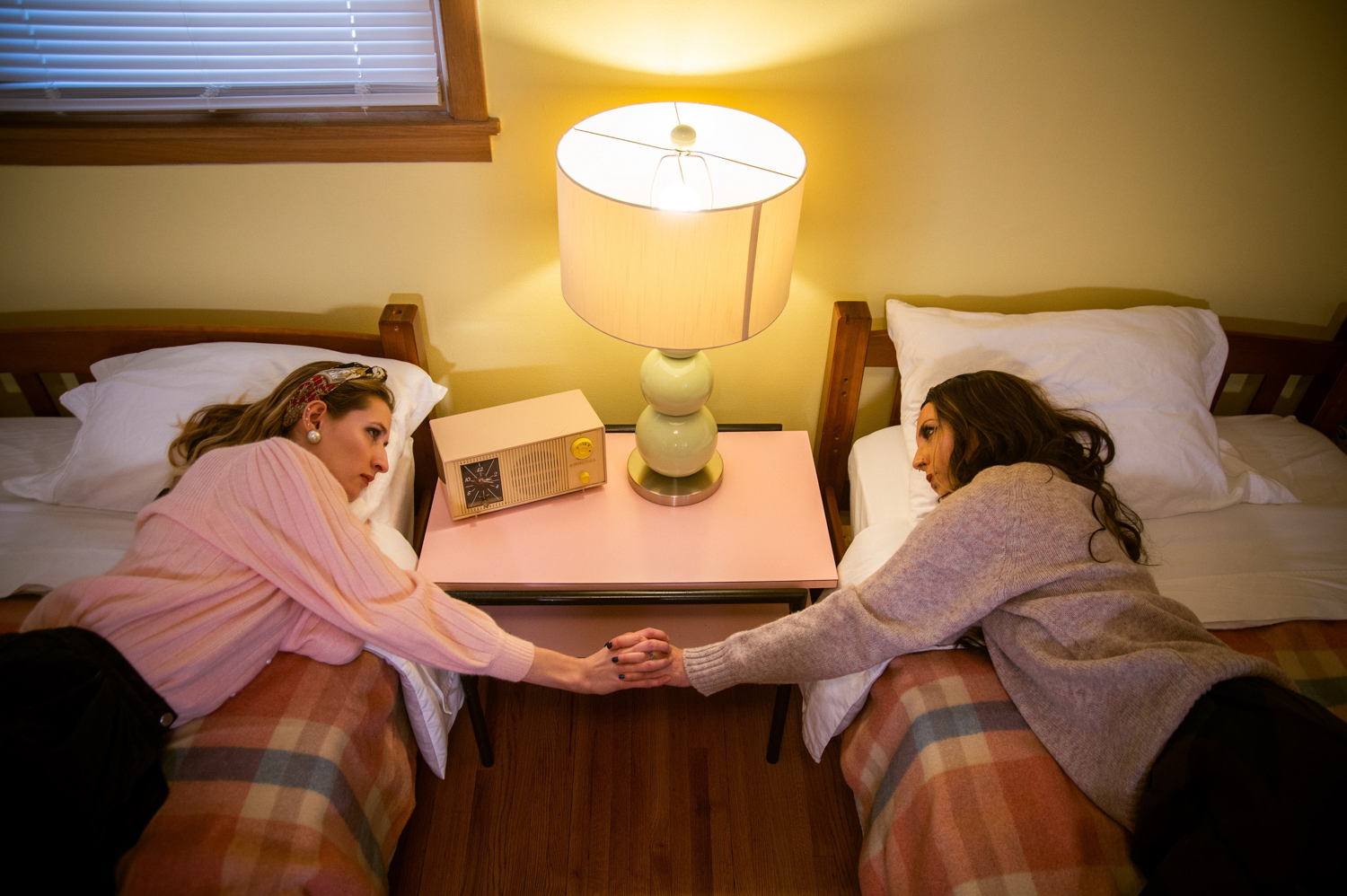 two girls lying on two twin beds holding hands looking at eachother